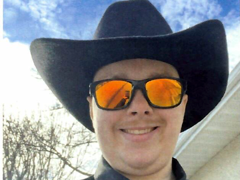Owen smiling in a black cowboy hat, orange mirrored sunglasses and a red tie