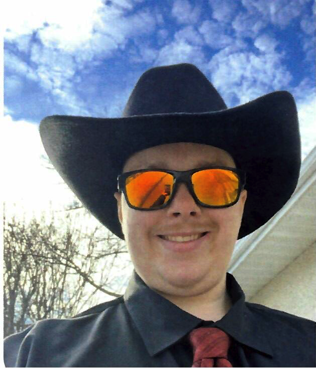 Owen smiling in a black cowboy hat, orange mirrored sunglasses and a red tie